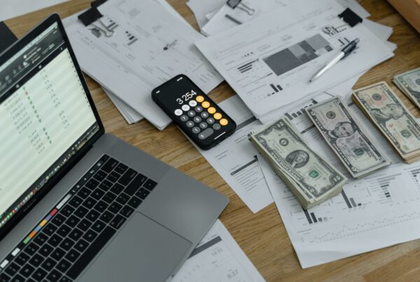 Stacks of US currency, financial reports, and a calculator on a desk with a laptop—representing long-term financial planning and wealth transfer