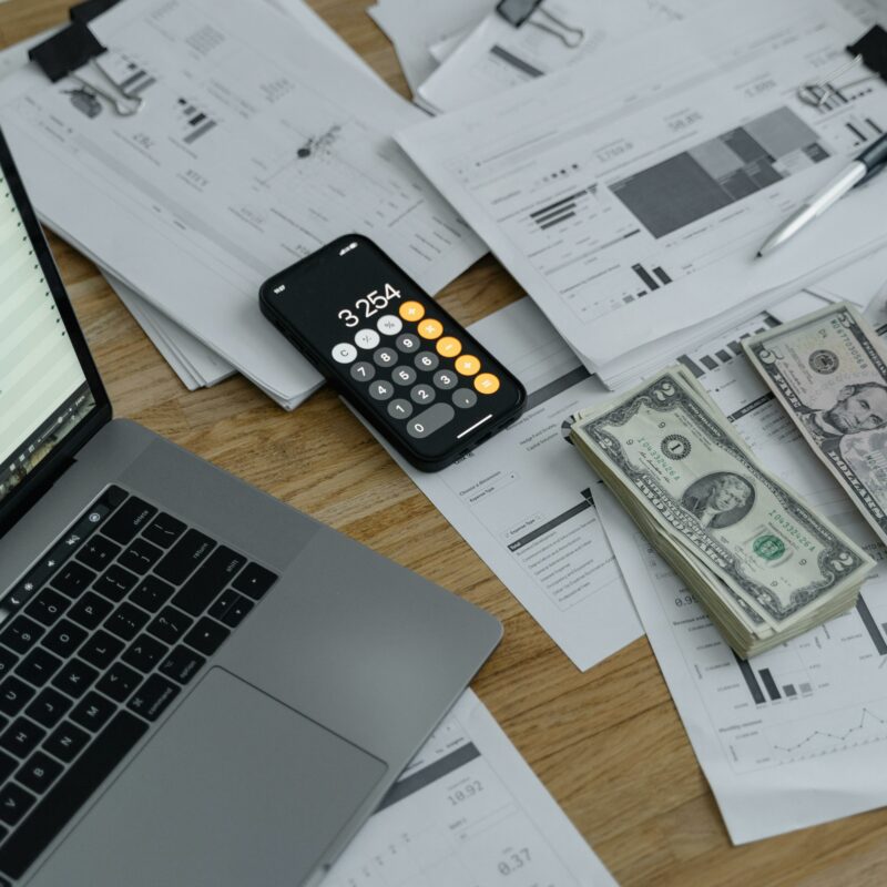 Stacks of US currency, financial reports, and a calculator on a desk with a laptop—representing long-term financial planning and wealth transfer