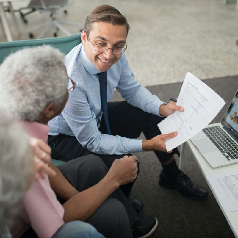 Financial advisor smiling and explaining paperwork to senior clients, representing retirement planning and addressing common misconceptions