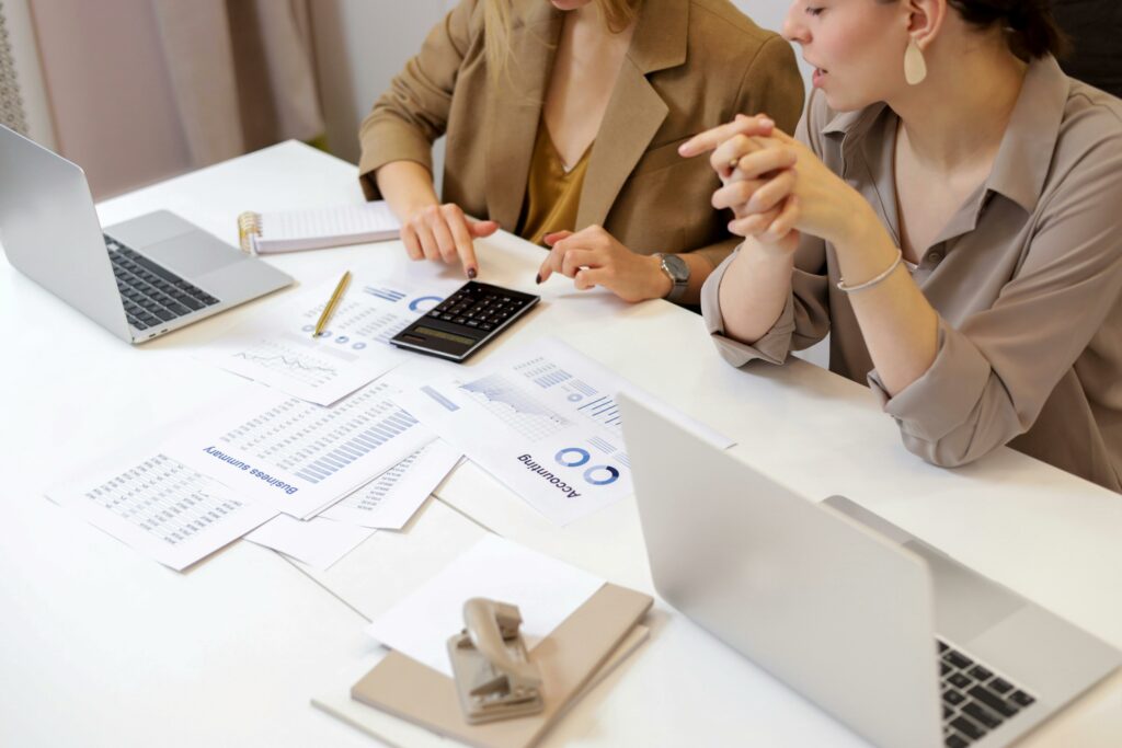 Two professionals reviewing financial reports and investment charts with laptops and a calculator, illustrating risk-managed investment planning