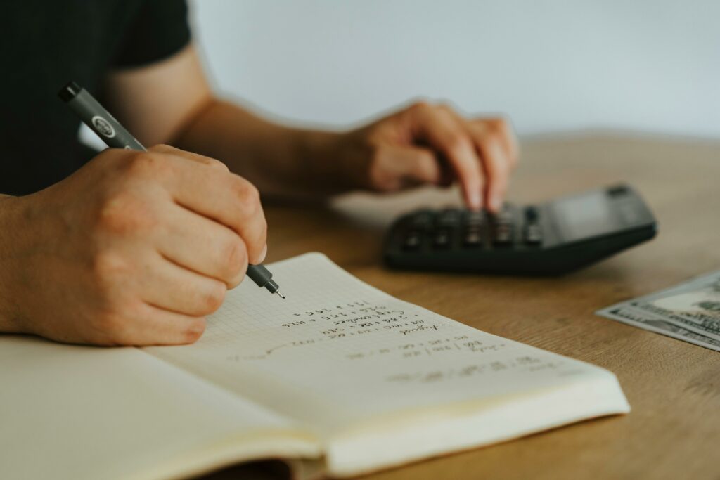 Close-up of a person writing in a financial notebook and using a calculator, symbolizing goal-oriented portfolio planning and personal finance strategy