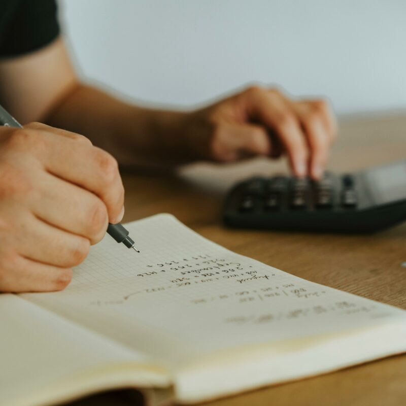 Close-up of a person writing in a financial notebook and using a calculator, symbolizing goal-oriented portfolio planning and personal finance strategy