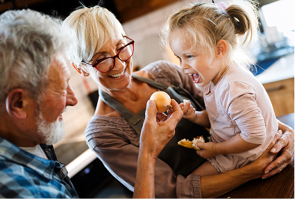 Joyful grandparents sharing a playful moment with their granddaughter in a kitchen, reflecting the values of family and long-term financial care